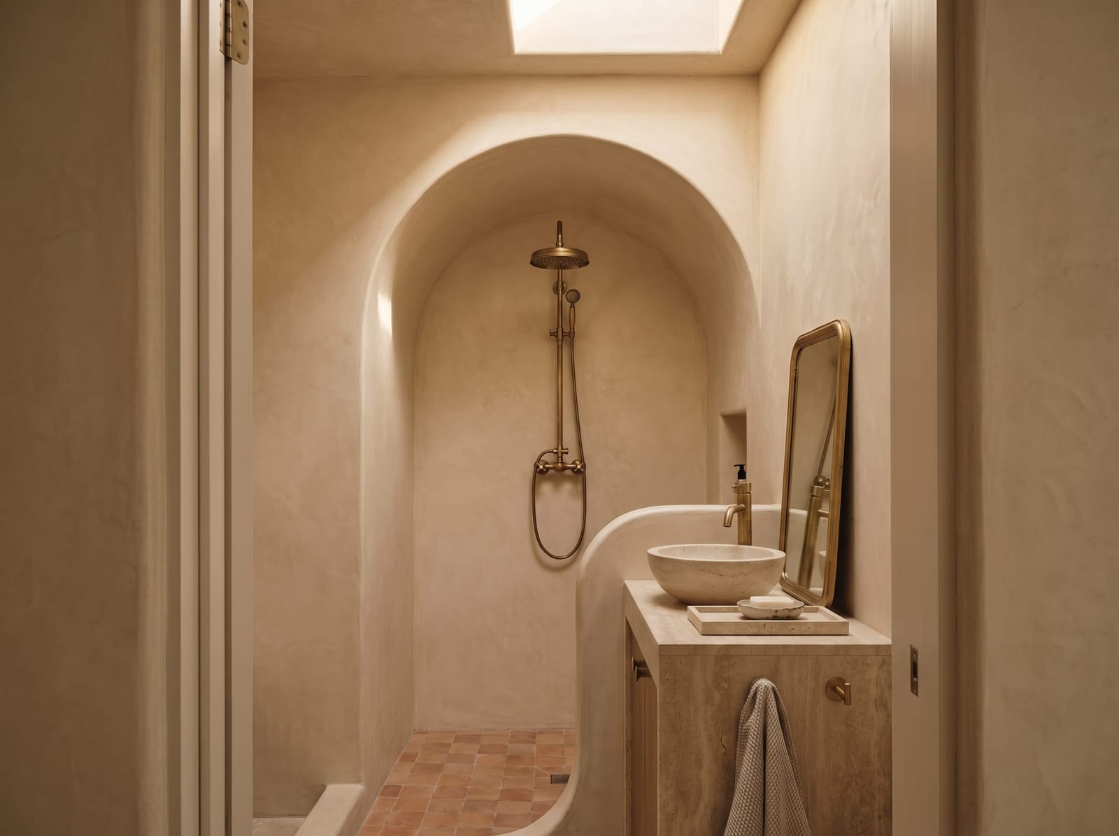 Horizontal view of the curved lime plaster arch walk-in shower and stone vanity area.