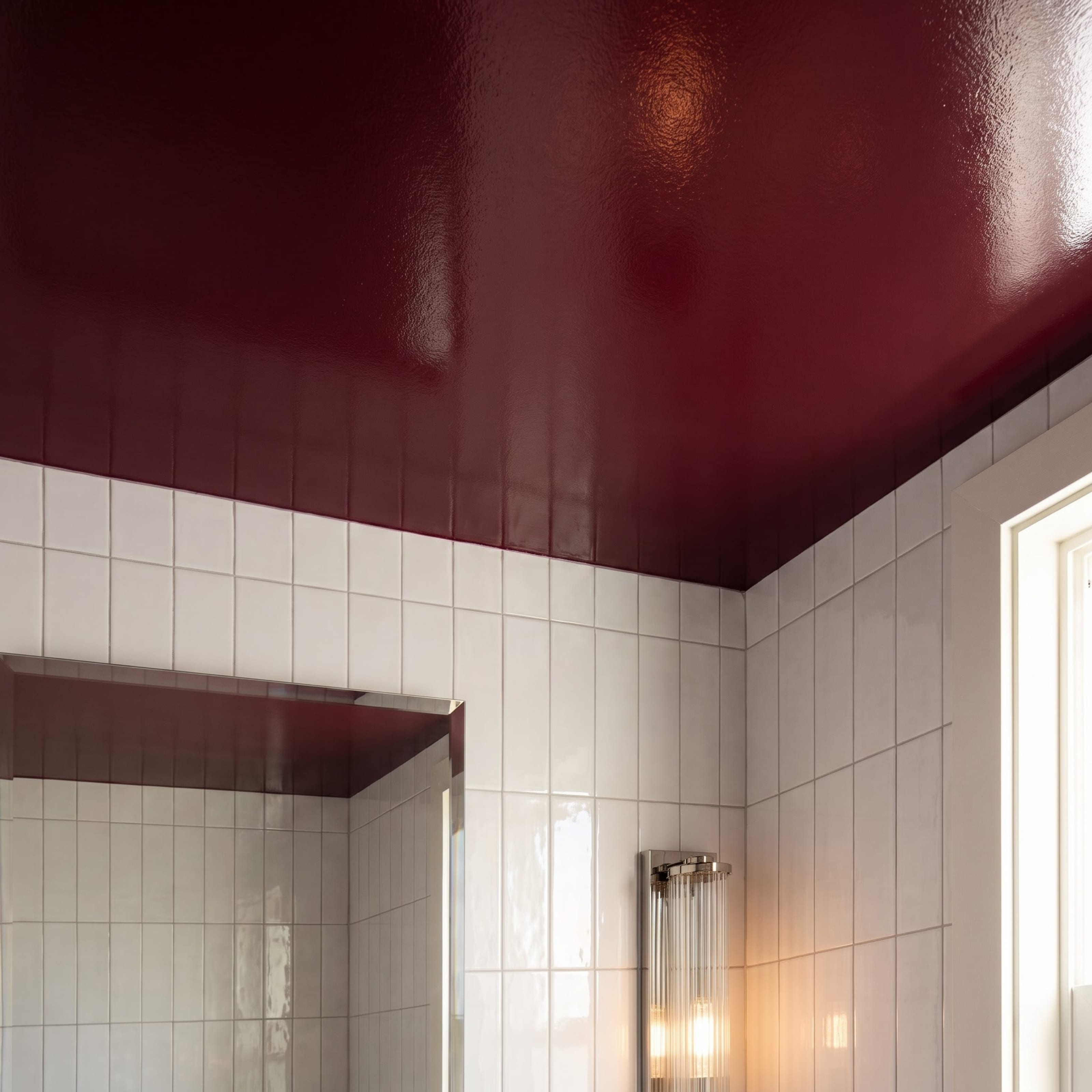 Close view of the glossy burgundy ceiling meeting vertically stacked warm-white tile in the powder room
