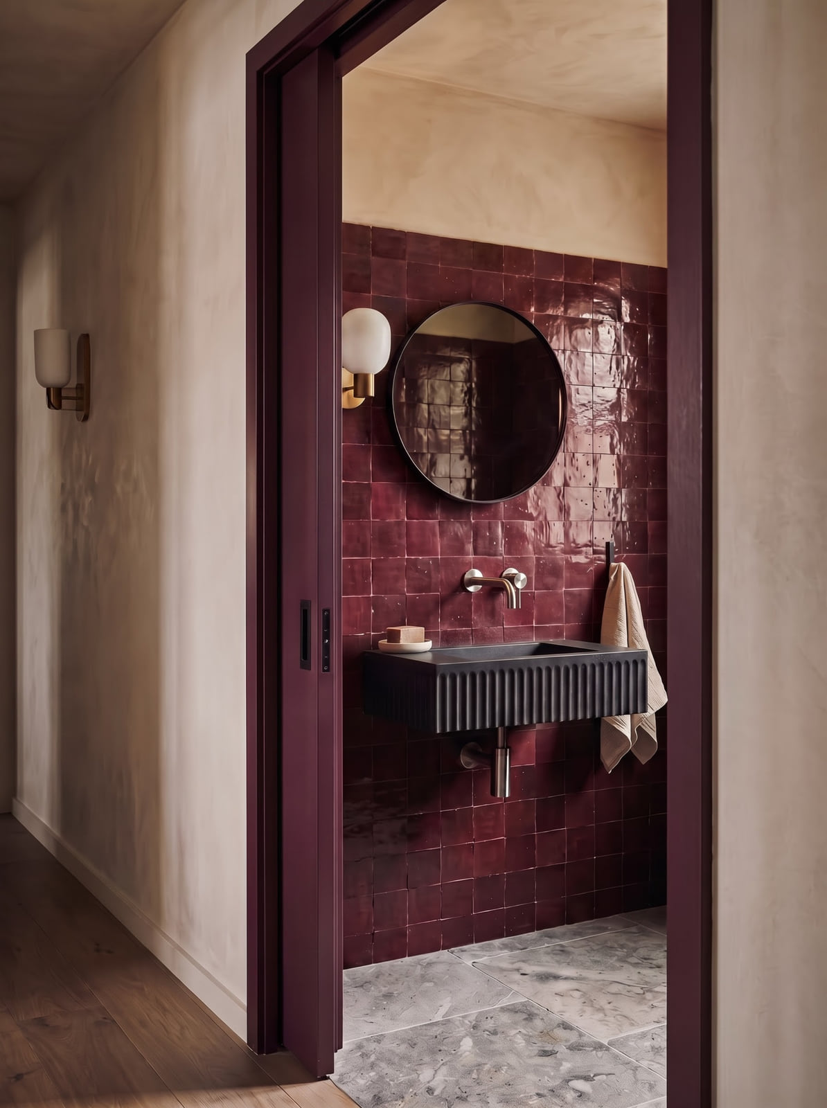 Burgundy tile powder room shown under soft natural daylight and warm evening sconce light.