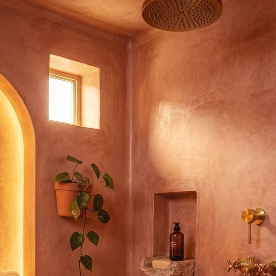 Close-up of a terracotta-colored plaster wall with hand-troweled texture beside a brass shower fixture.