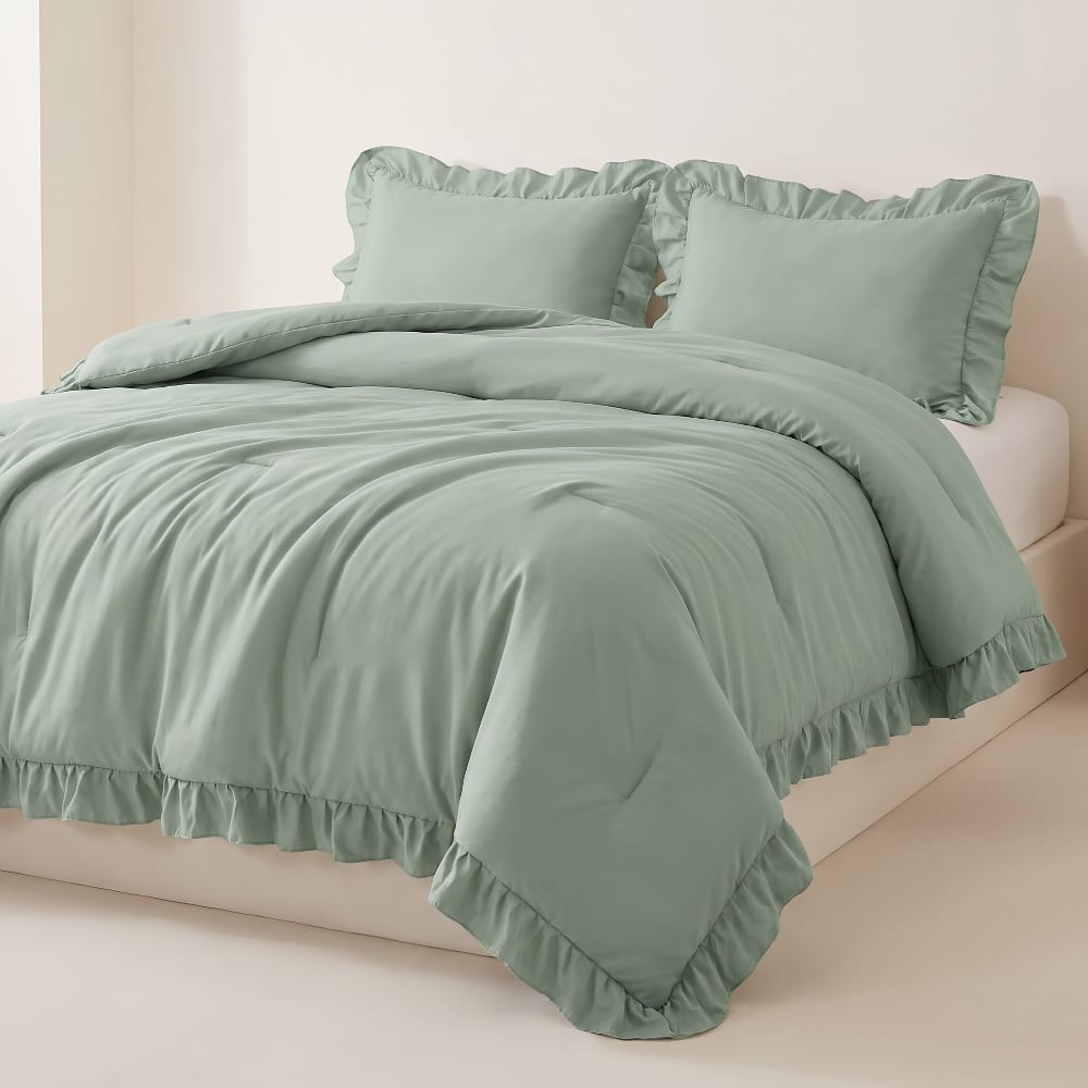 Sage green ruffled comforter and two ruffled shams on a bed against a cream wall