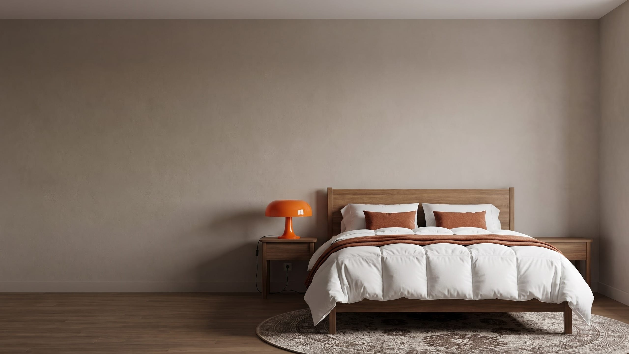 Bedroom with a white box-stitched comforter, rust cushions and throw, an orange glass mushroom lamp on a wood nightstand and a brown medallion round rug.