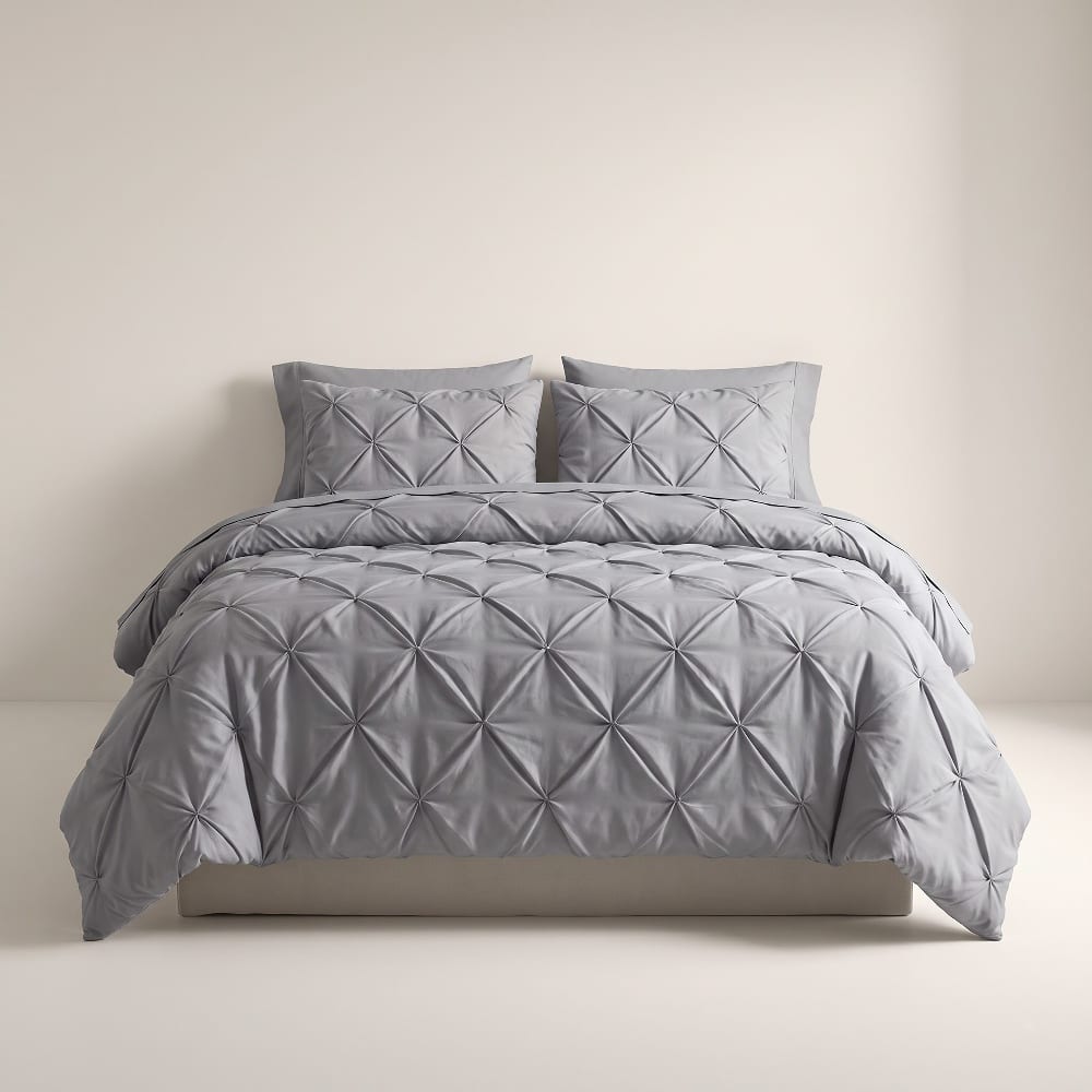 Gray pintuck comforter with diamond pinch pleats and matching shams on a made bed