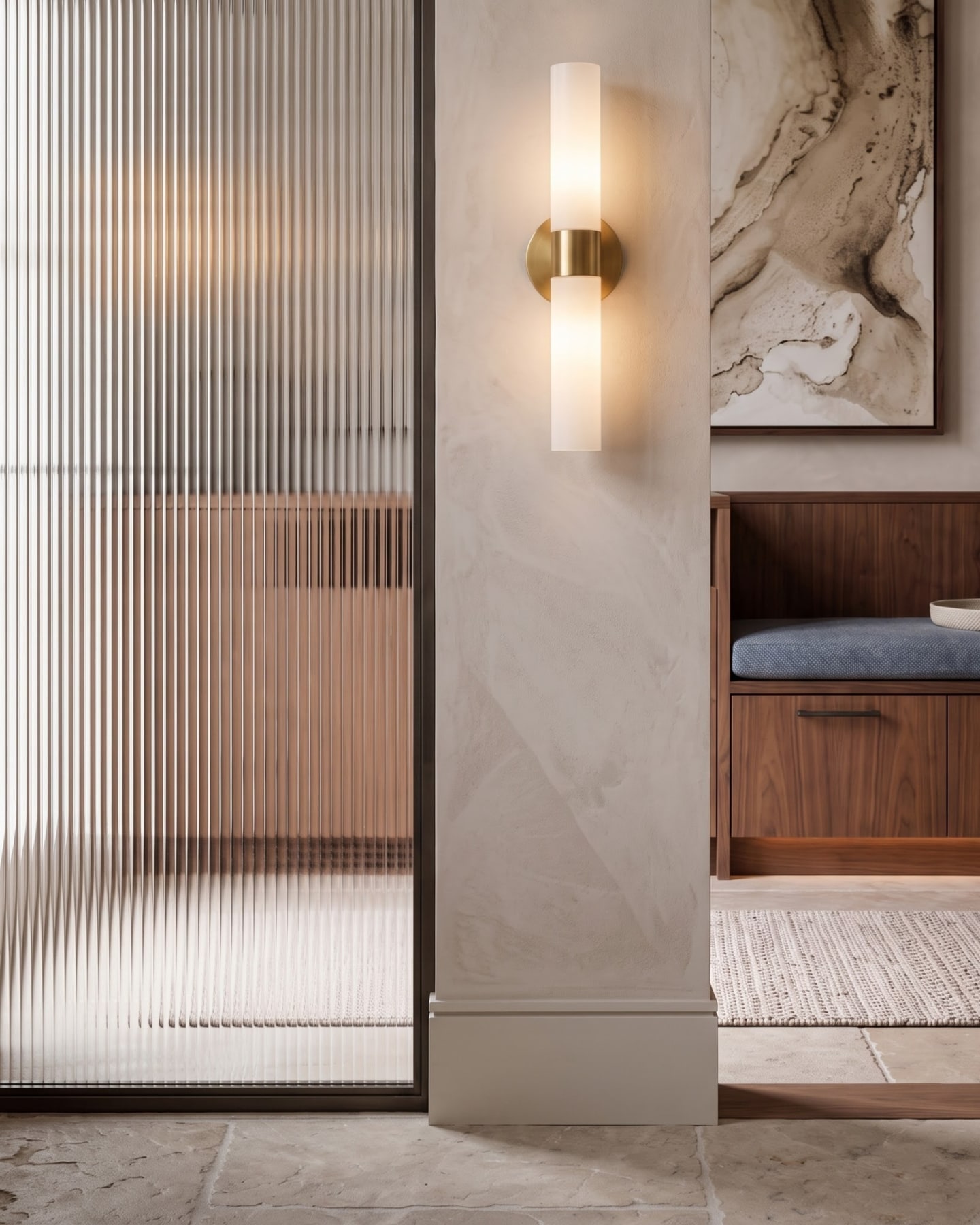 Ribbed glass partition framed in dark metal alongside an illuminated brass tube sconce and walnut bench.