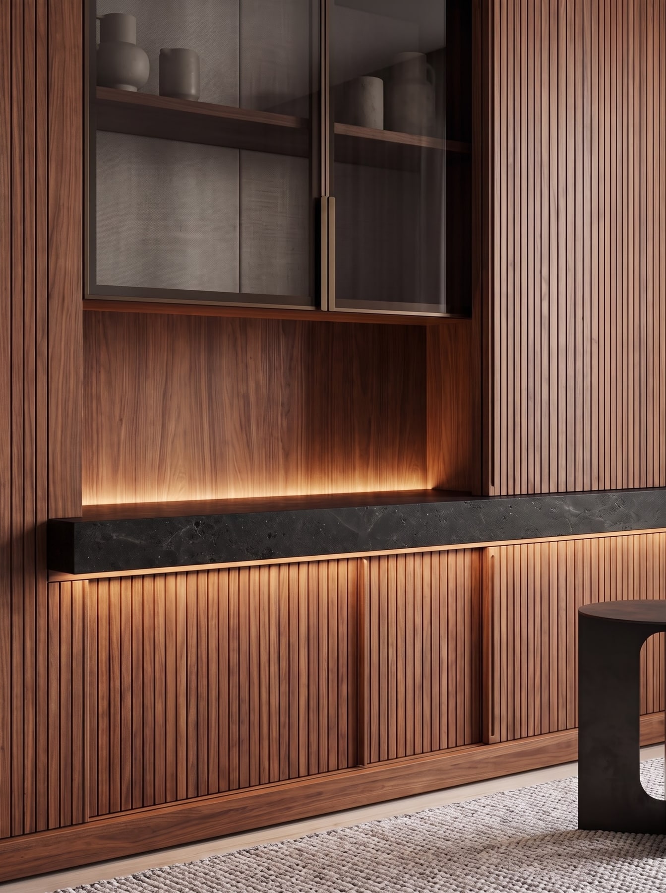 Fluted walnut cabinet with integrated dark stone countertop, warm LED accent lighting, and upper glass-front display cupboards.