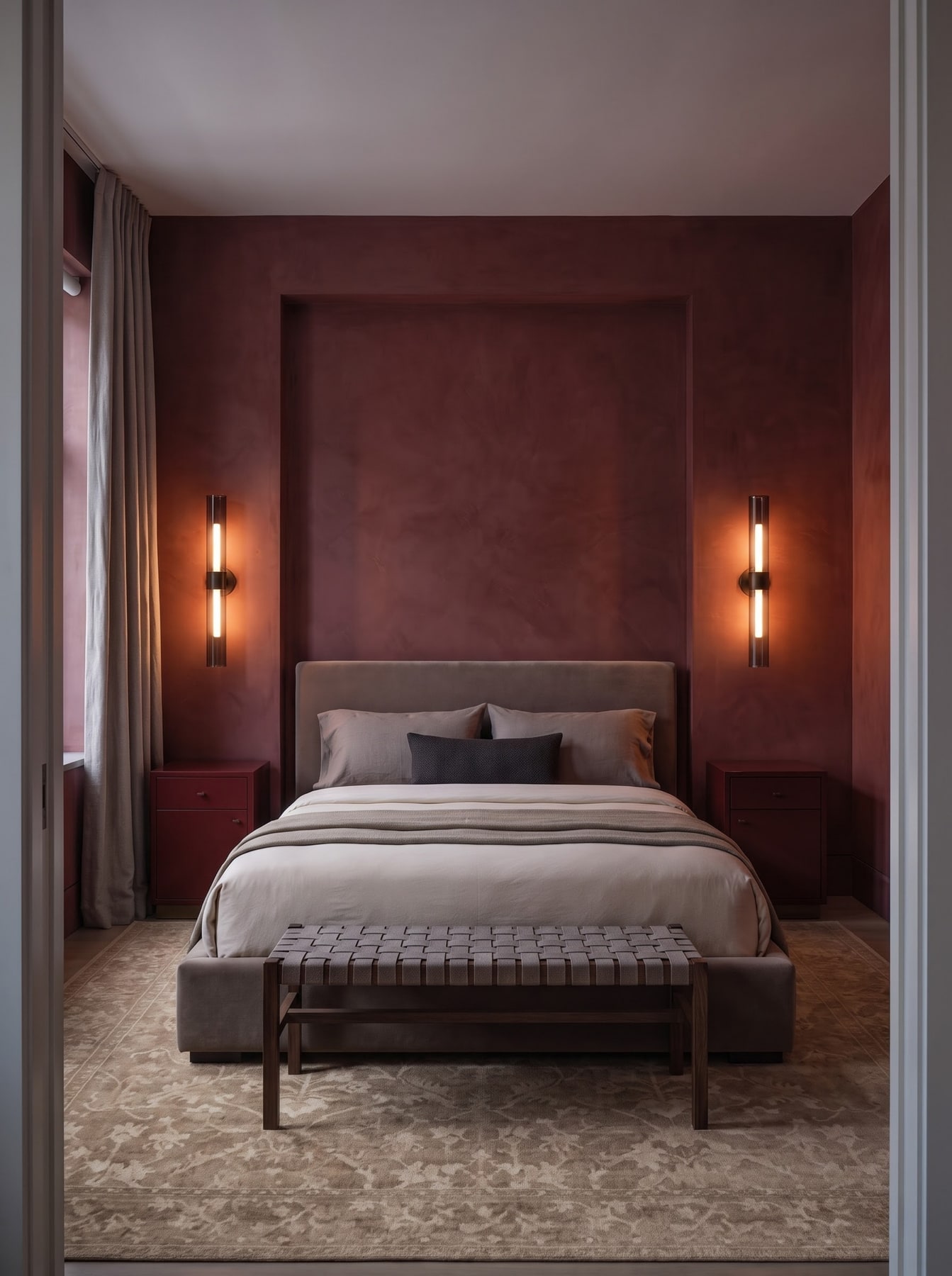 Deep oxblood bedroom with lime-washed recessed wall, upholstered bed, matching nightstands, and vertical glowing wall sconces.