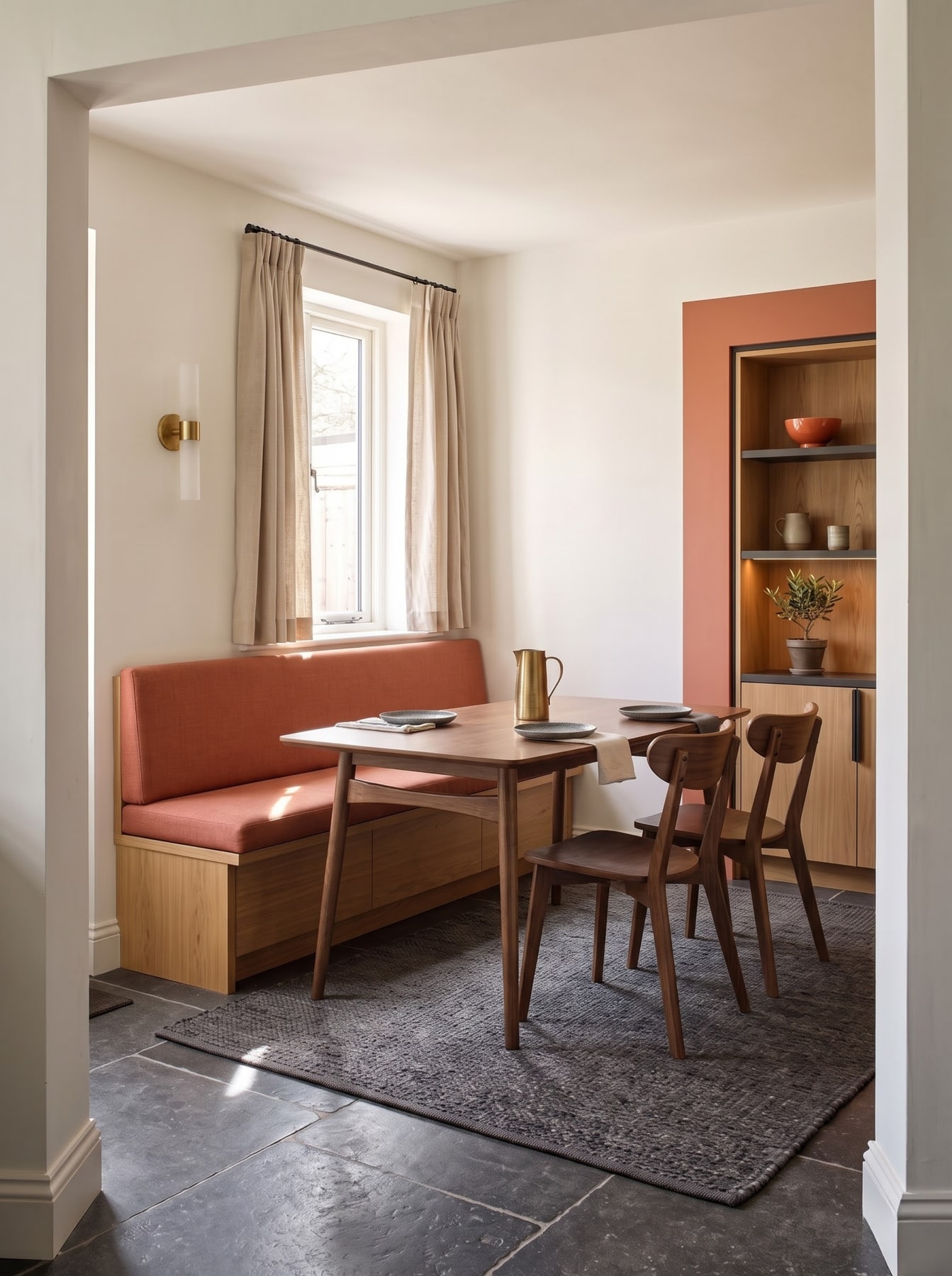 Dining corner with a terracotta cushioned bench, timber table and chairs, and a matching terracotta-framed built-in shelving alcove.