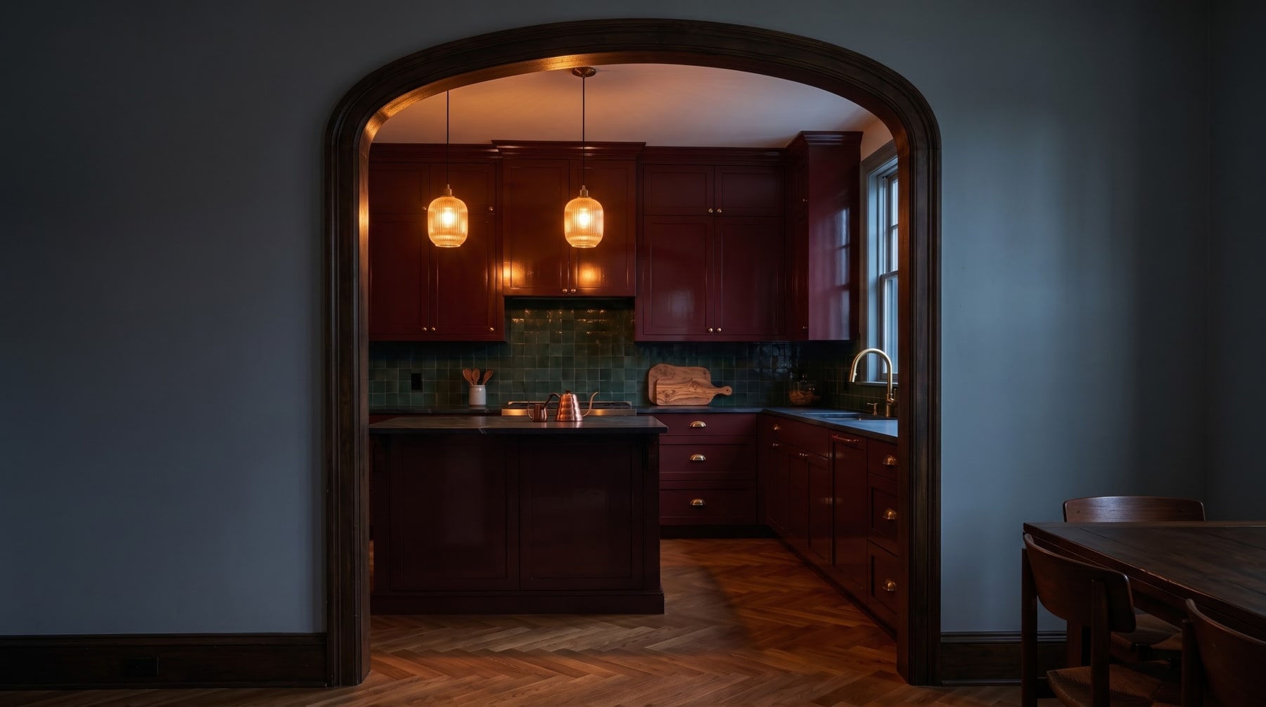 Wide view through a timber archway into a deep plum kitchen with glossy green backsplash and warm pendant lights.