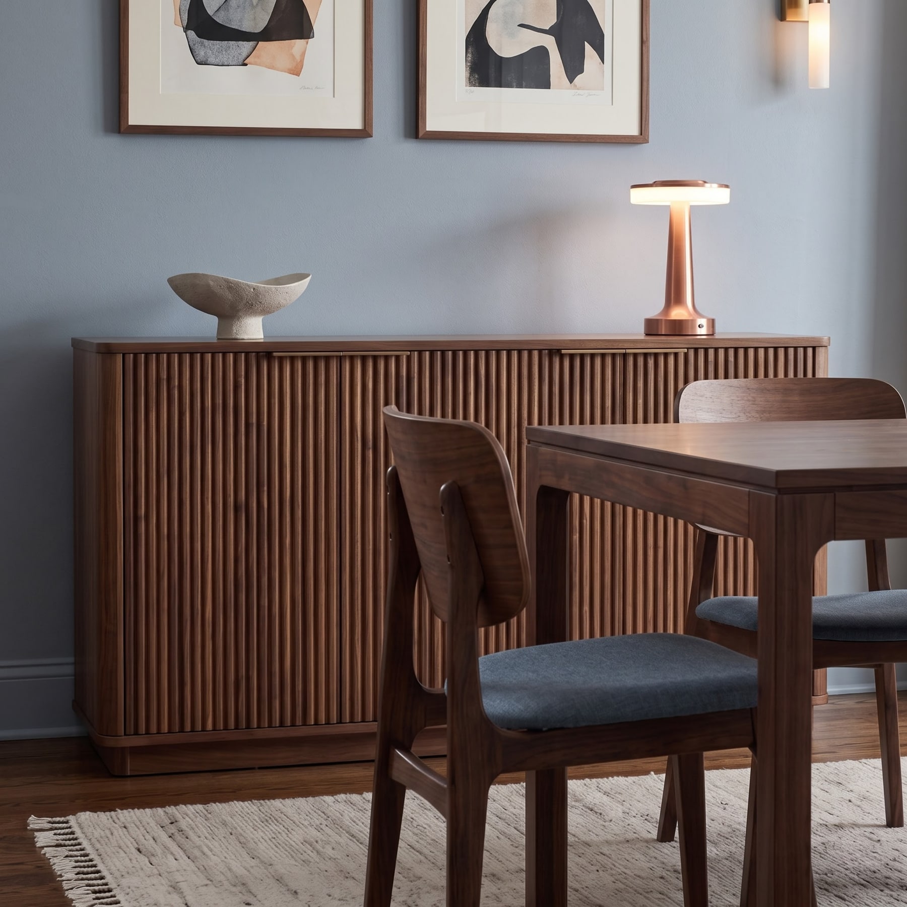 Fluted walnut sideboard with sculptural bowl and lamp, beside a timber dining table with upholstered chairs on light rug.